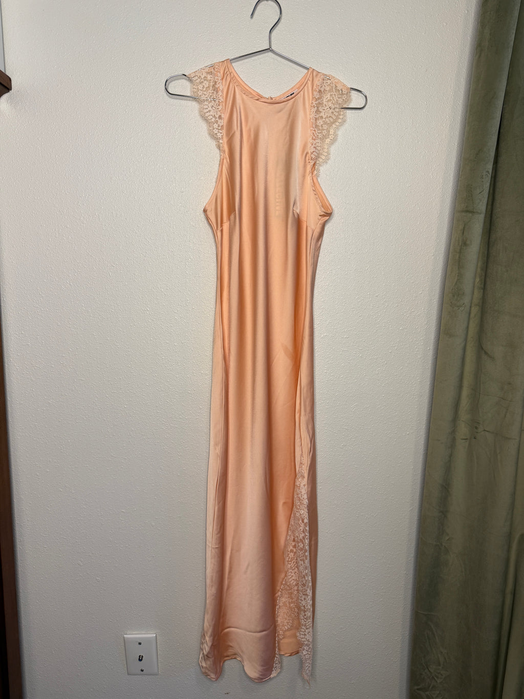 Pink dress with lace details on a hanger against a plain wall.