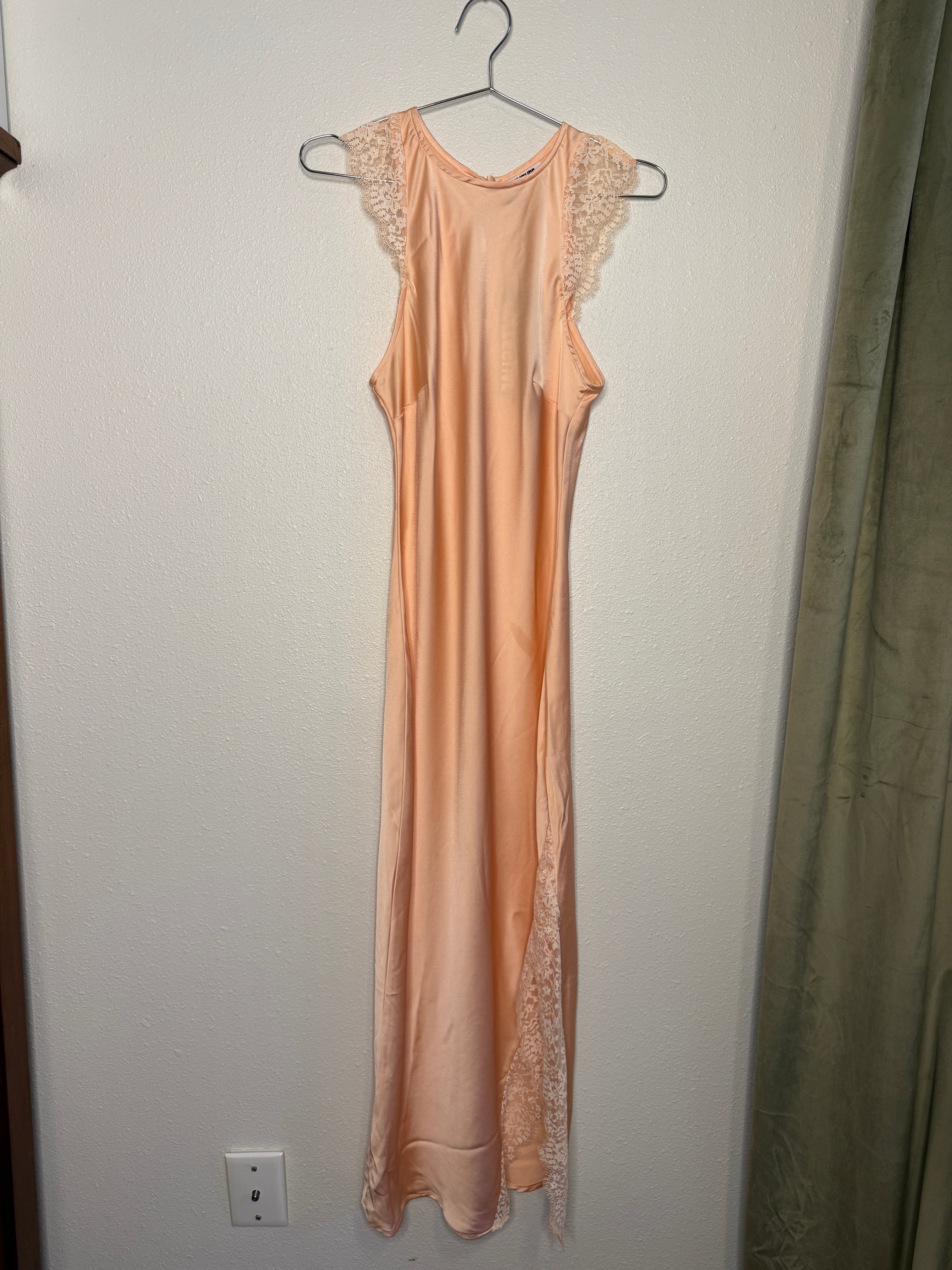 Pink dress with lace details on a hanger against a plain wall.