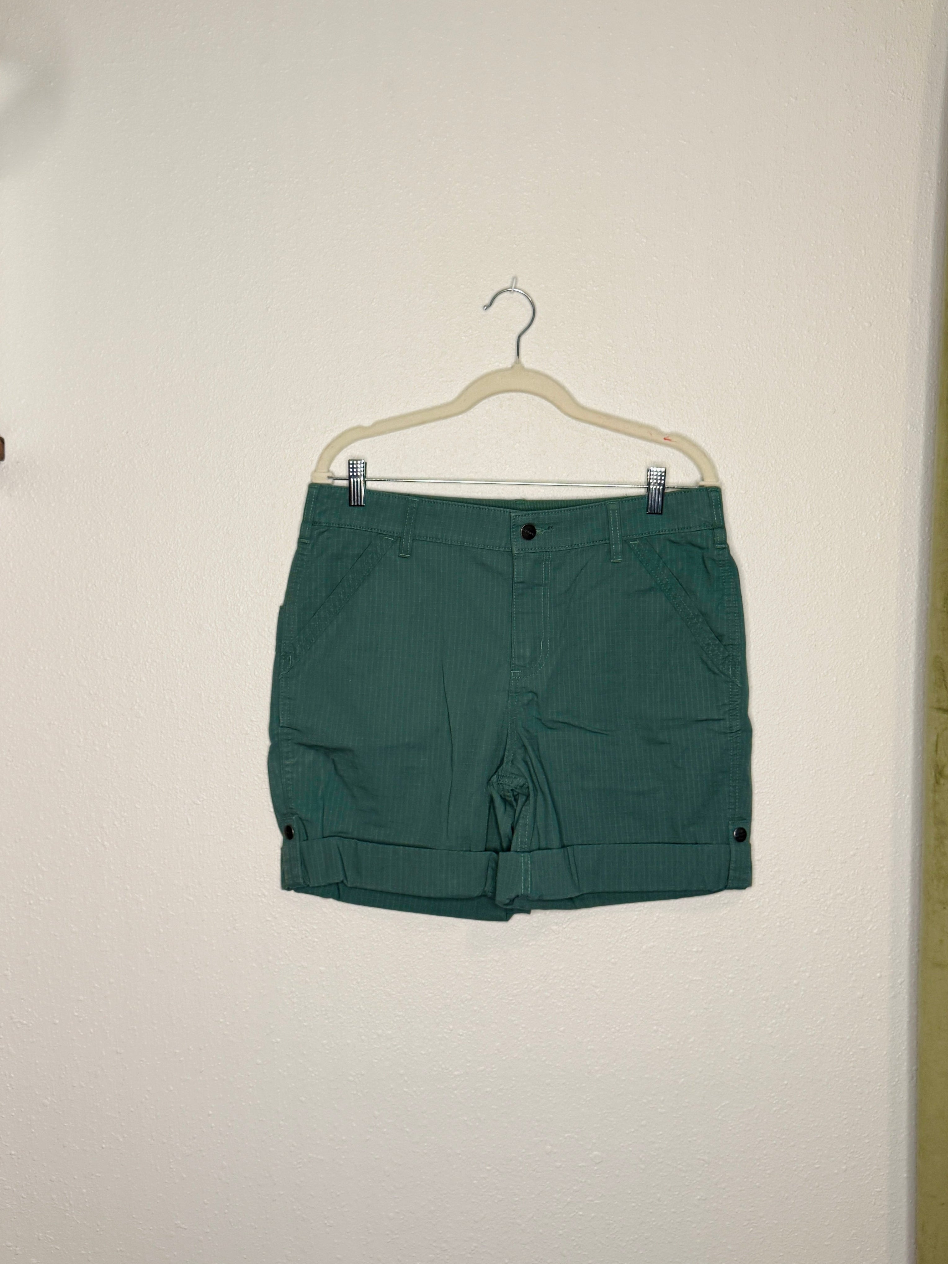 Green shorts hanging on a hanger against a white wall.