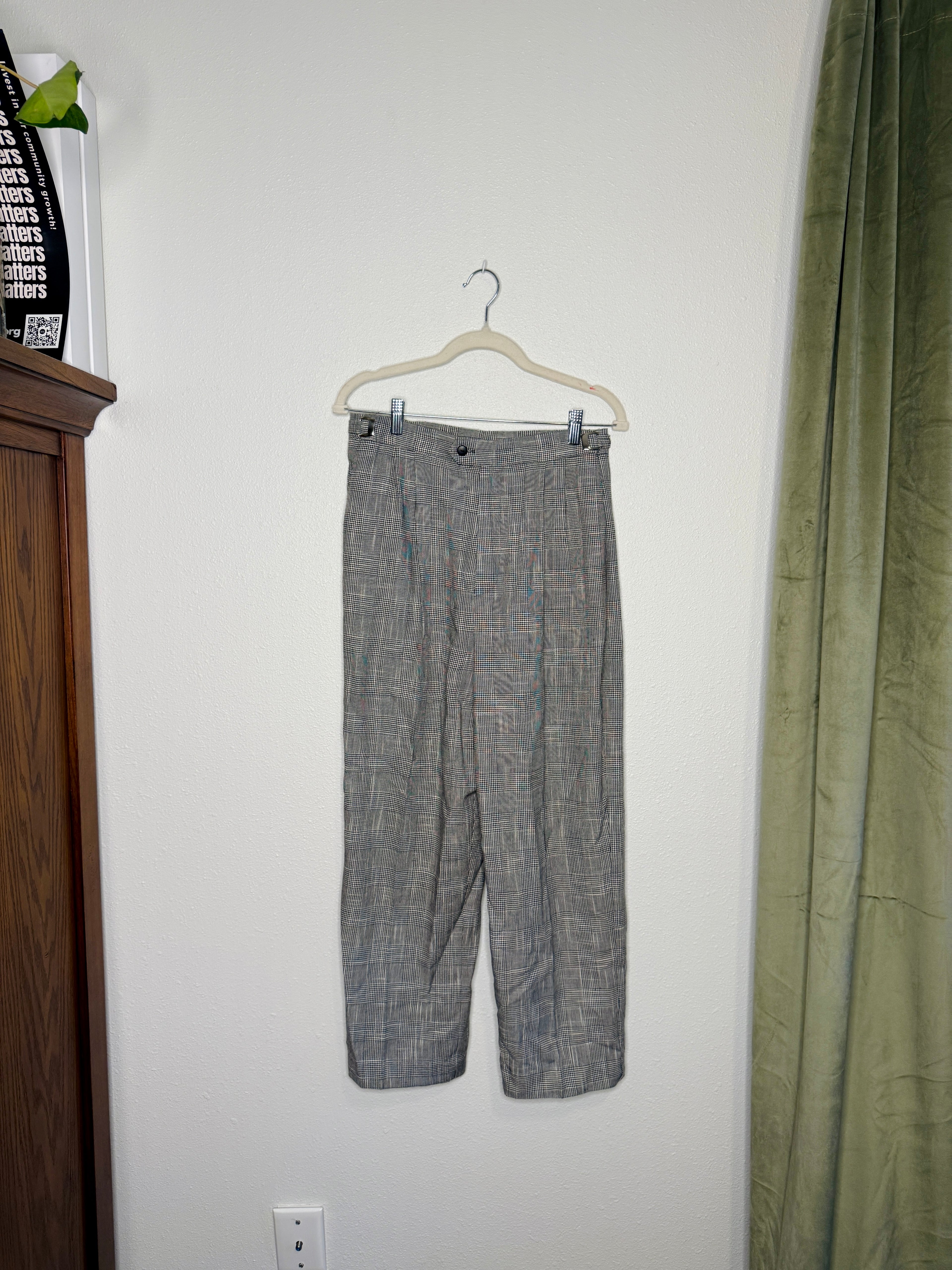 Gray checkered pants on a hanger against a white wall.