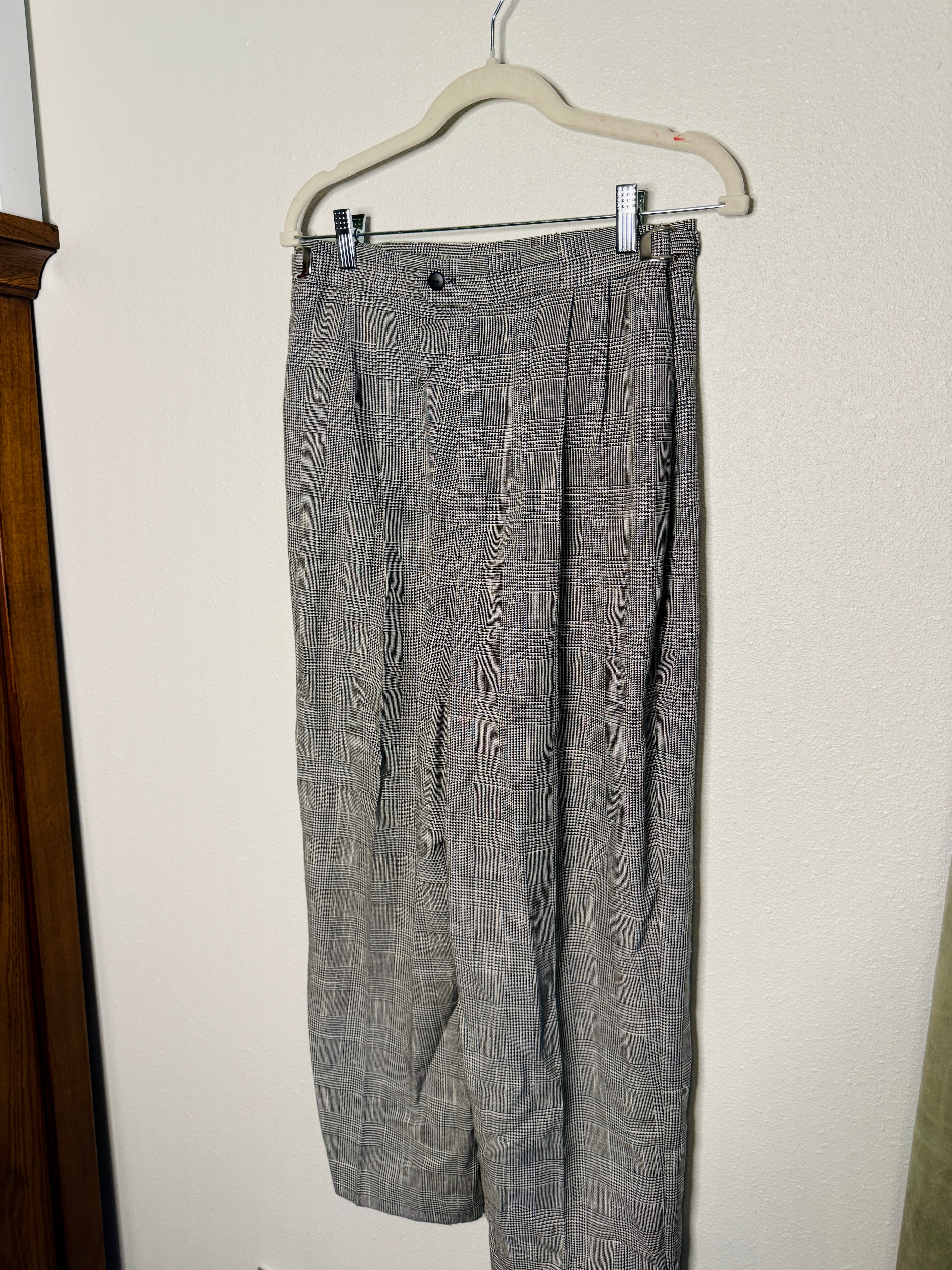 Gray checkered pants hanging on a white hanger against a white wall.
