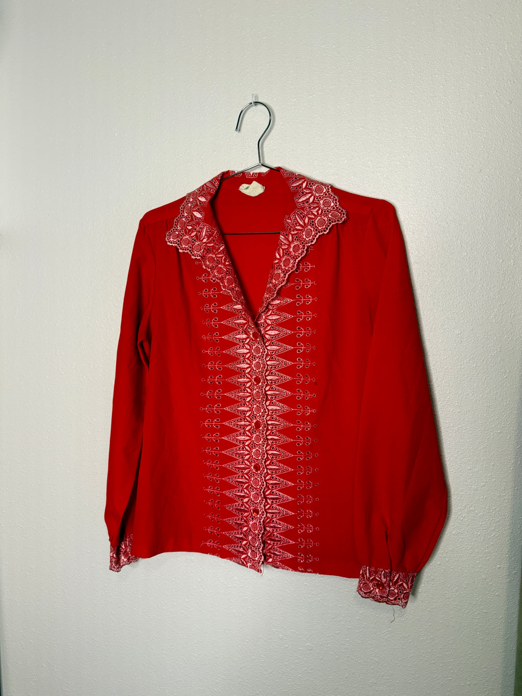 Red blouse with intricate white embroidery on a hanger against a plain background