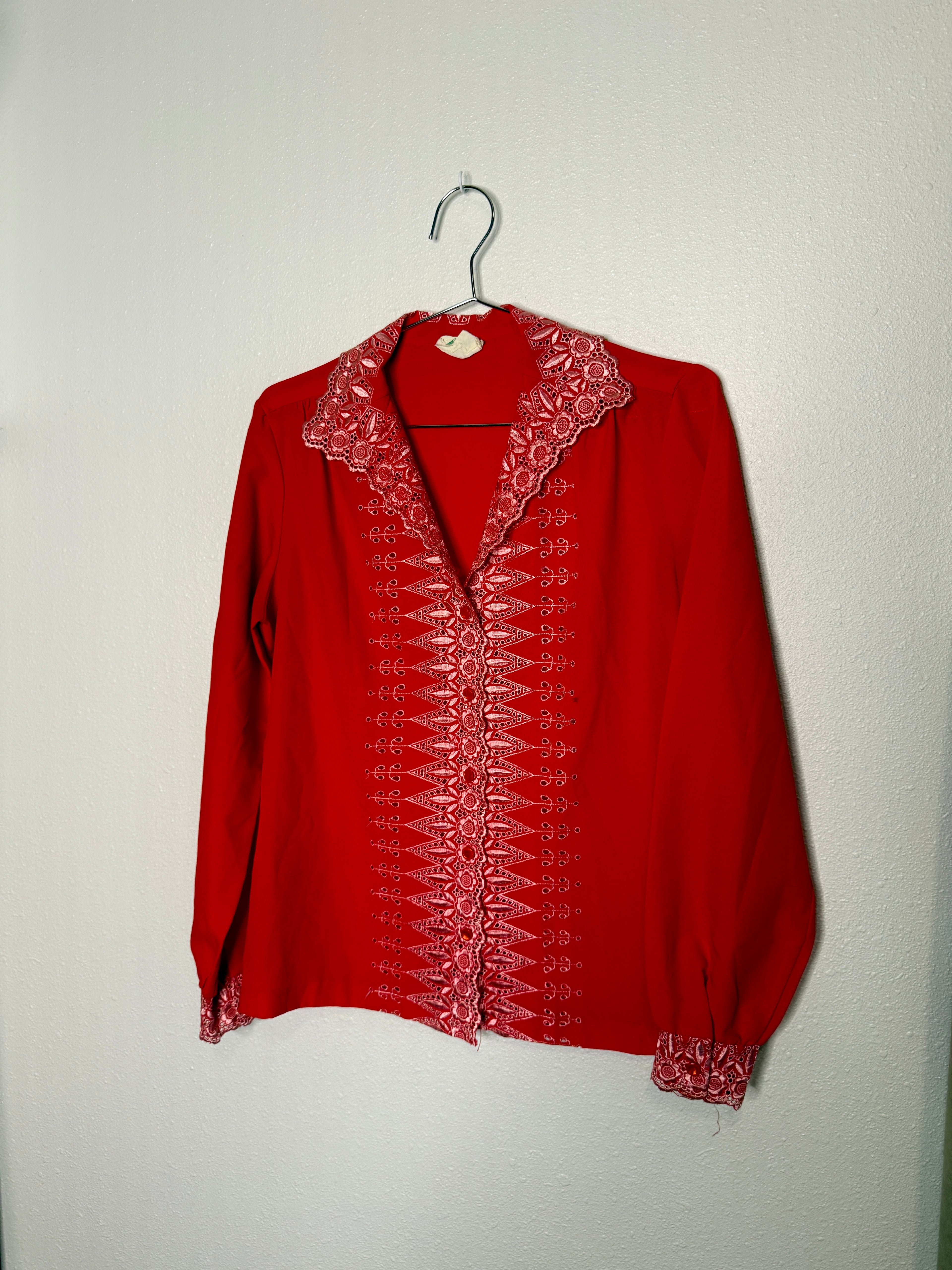 Red blouse with intricate white embroidery on a hanger against a plain background