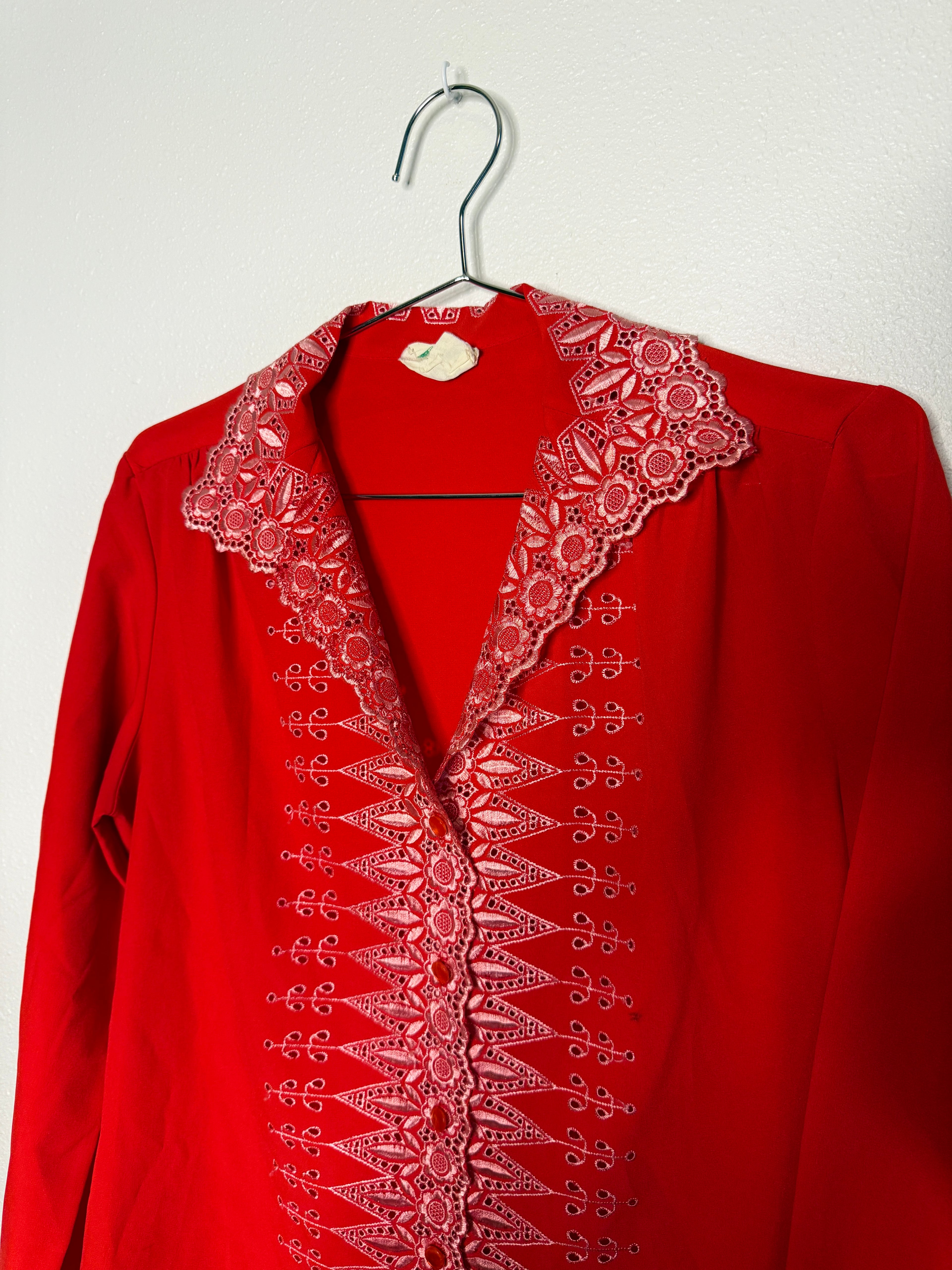 Red blouse with intricate lace detailing on a hanger against a white background